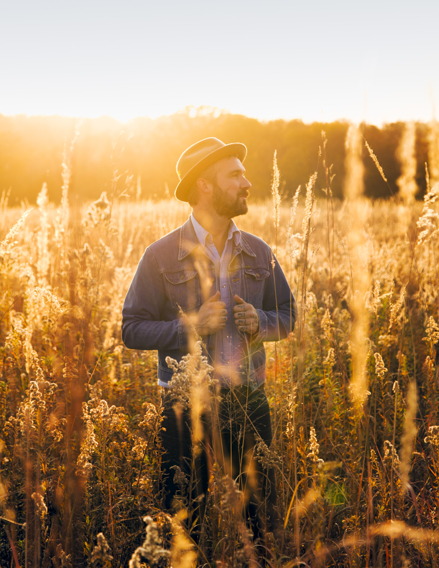 A portrait of a man standing in a grassy field at sunset by Washington DC photographer Ryan Donnell