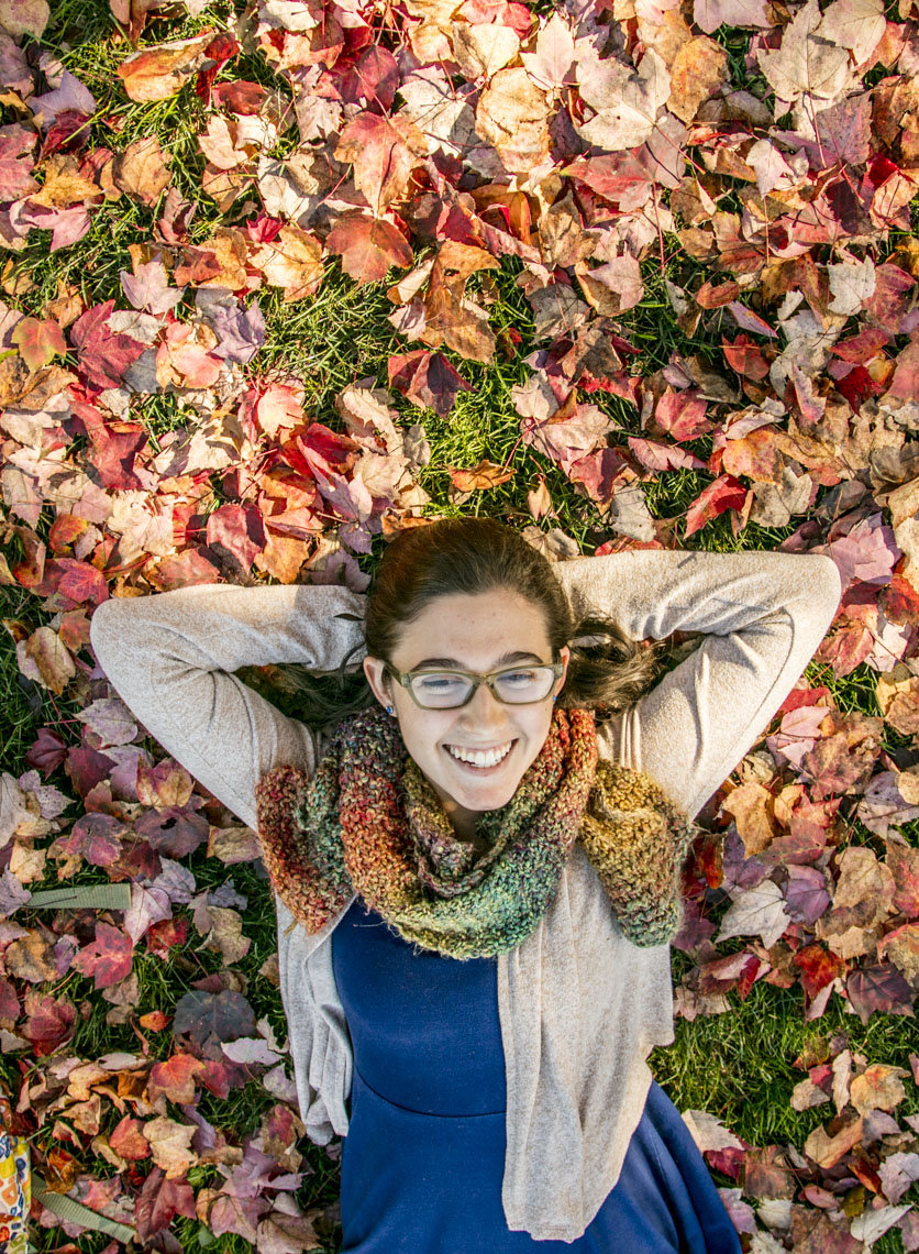 A female college  student relaxes in fallen fall foliage in a photo by Ryan Donnell