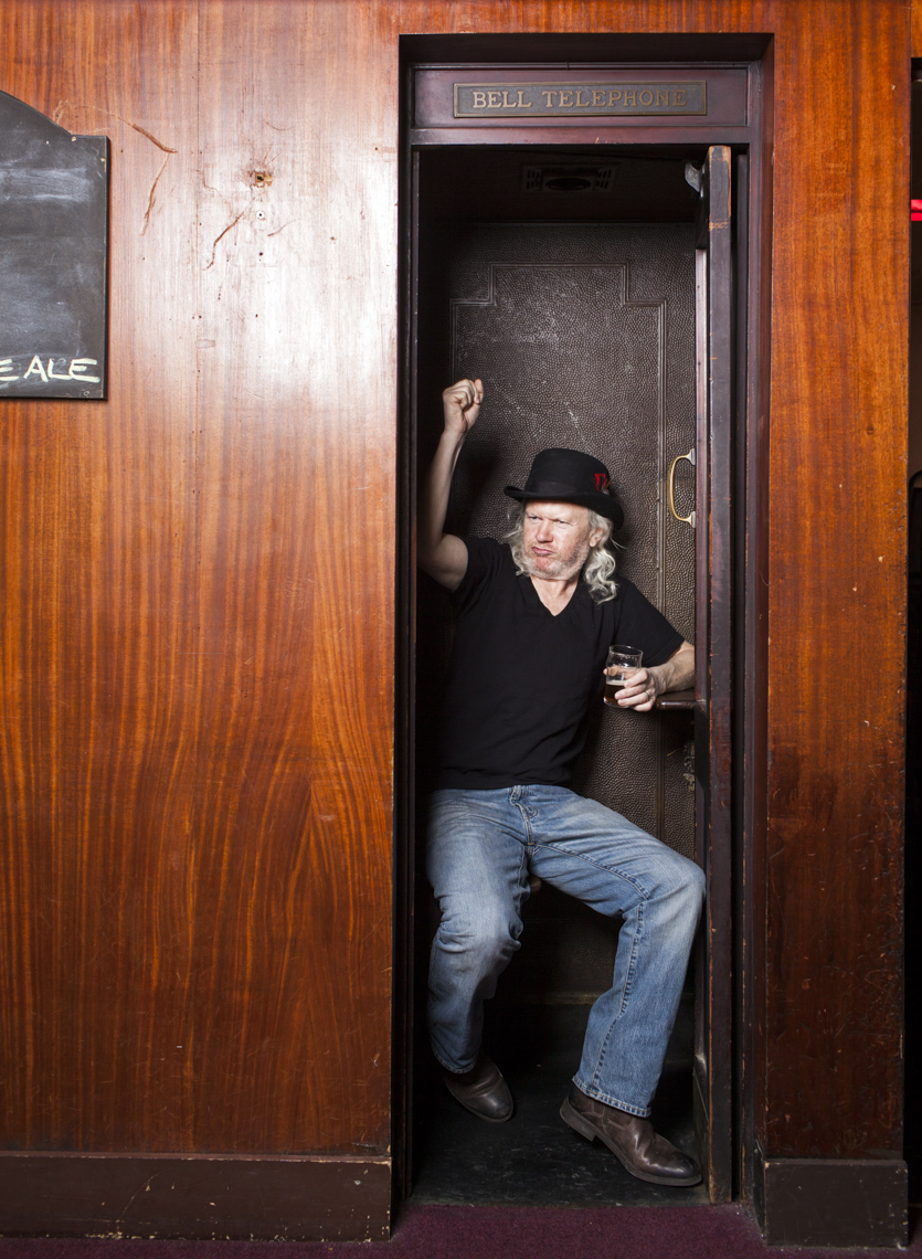 An editorial portrait of a bar owner sitting in a phone booth drinking a beer by Washington DC photographer Ryan Donnell