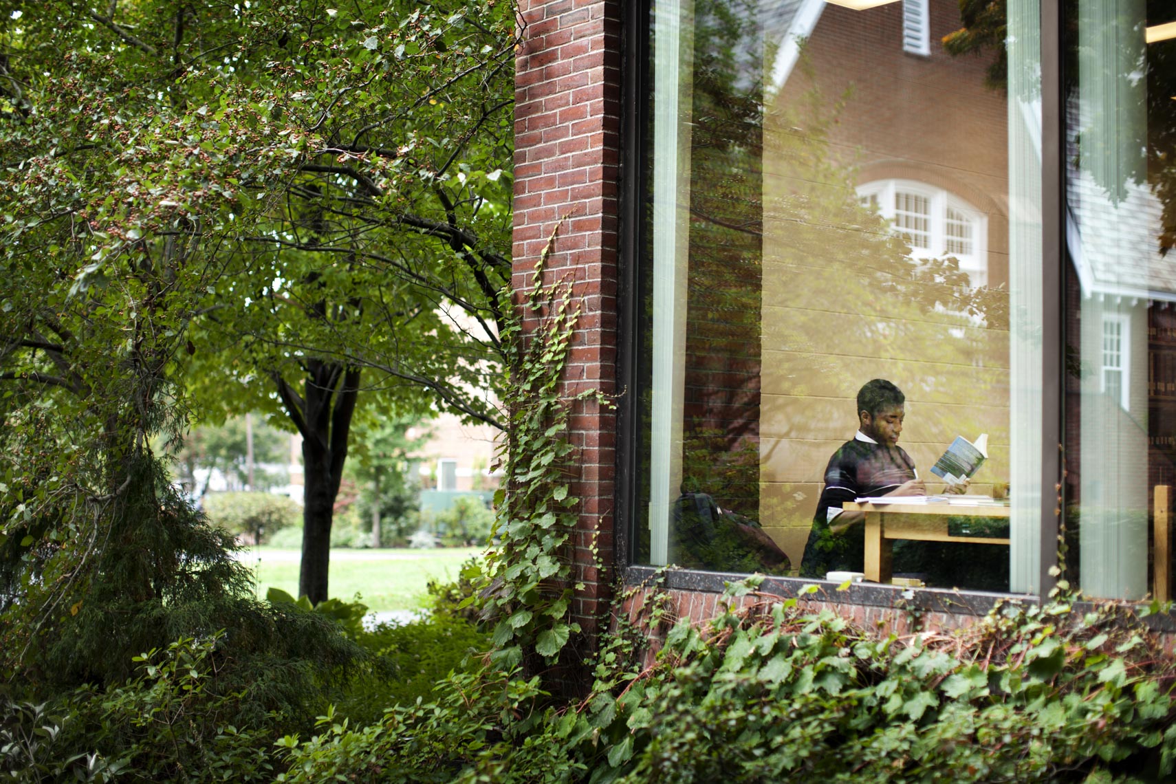 A student studies in a college campus library as seen from the outside at dusk in a photo by Ryan Donnell
