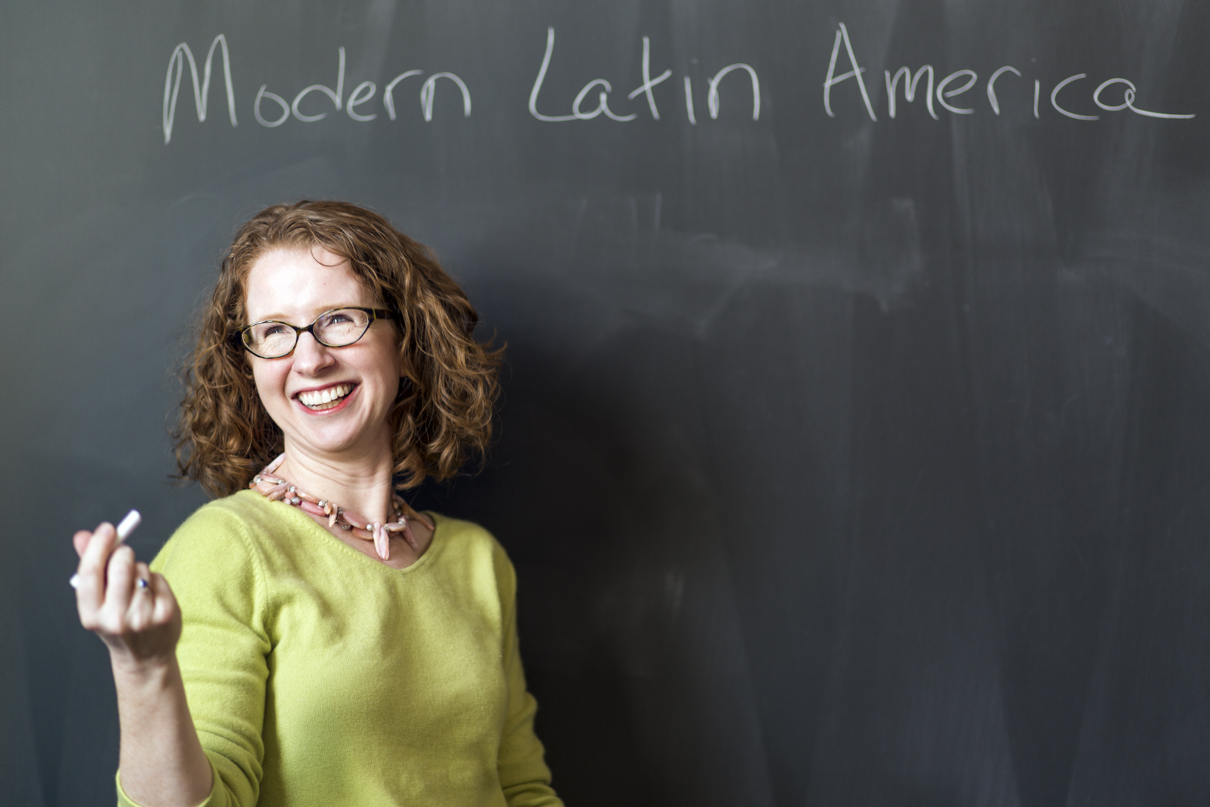 A college professor laughs while standing in front of a chalkboard in a photo by Ryan Donnell